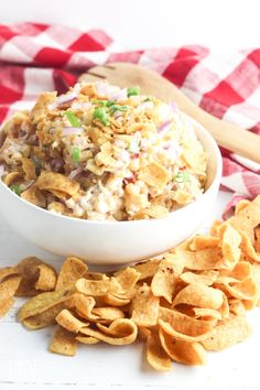 a white bowl filled with coleslaw and chips on top of a checkered table cloth