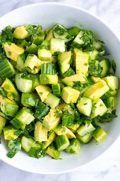 a person holding a spoon in a bowl filled with cucumber and avocado