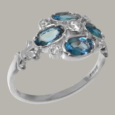 "A romantique style nine stone ring with delicate fleur de lis design on the shoulders. the London Blue Topaz are 5x4mm oval shaped, the center Cubic Zirconia are 2.75mm and 1.5mm round. We use Natural Topaz which have been carefully chosen for this ring by expert Jewellers to ensure a good fit. The London Blue Topaz stone has a beautiful and mezmerising ocean blue colour which is elevated by the sparkle of these clear white Cubic Zirconia enhancing the London Blue Topaz and unveiling their full Red Ring Box, Blue Topaz Stone, Vibrant Blue, London Blue Topaz, Natural Sapphire, London Blue, Sapphire Diamond, Real Diamonds, Cluster Ring