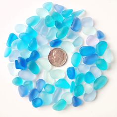 a penny sitting on top of a pile of blue and white sea glass pieces next to each other