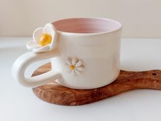 a white coffee cup sitting on top of a wooden board with a flower in it