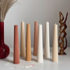 several different colored vases sitting next to each other on a white table with a plant in the middle