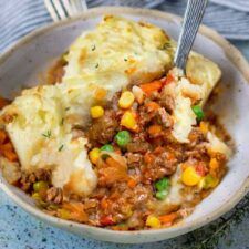 a bowl filled with mashed potatoes, meat and veggies next to a fork