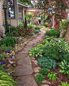 a stone path in front of a house with lots of plants and flowers around it