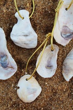 three seashells are on the sand and one is hanging from a gold wire