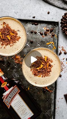 two glasses filled with drinks sitting on top of a metal tray next to coffee beans