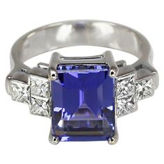 This S.Georgios designer Ring is all hand-made in 18 Karat White Gold and features a stunning Spotless Emerald cut natural Tanzanite total weight 6.01 Carat, surrounded by 6 princess cut VVS1 clarity and color F white Diamonds total weight of 0.88 Carat. This gorgeous and classic ring can also be ordered in yellow or Rose gold and with a different stone selection, please contact us. It comes with a Photographic Certificate of Quality Guarantee for Insurance and Valuation. All Georgios Collection 6 Princess, Tanzanite And Diamond Ring, Tanzanite Diamond Ring, Tanzanite Diamond, Natural Tanzanite, Classic Ring, White Diamonds, Princess Cut, Solitaire Ring