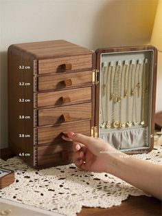 a wooden jewelry box with several drawers and gold necklaces in it, sitting on a lace doily