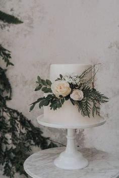 a white wedding cake with flowers and greenery on top sitting on a marble table