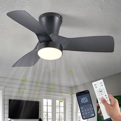 a person holding a remote control in front of a ceiling fan that is turned on