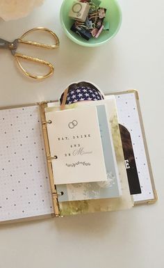 an open planner book sitting on top of a table next to a bowl of flowers