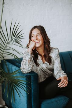 a woman sitting on top of a blue couch next to a potted palm tree