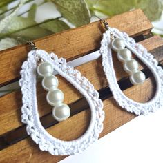 white crochet earrings with pearls hanging from them on a wooden stand next to leaves