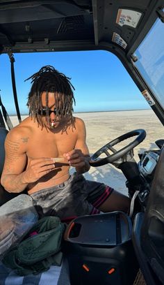 a shirtless man sitting in the drivers seat of a truck looking at his cell phone