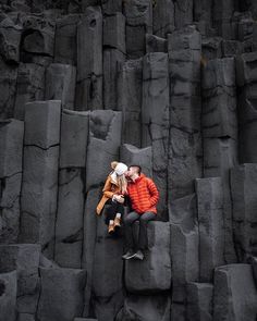 a man and woman sitting on top of a large pile of rocks next to each other