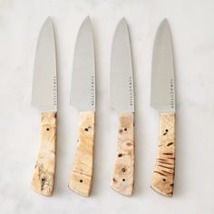 three knives are sitting next to each other on a white counter top, one is cut in half and the other has a wooden handle