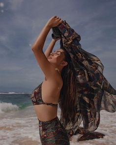 a woman standing on the beach with her arms in the air and wearing a bathing suit