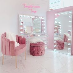 a pink chair sitting in front of a mirror with lights on the wall behind it