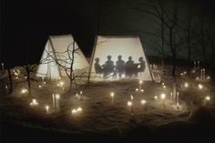 three people are standing in front of some tents with candles on the ground at night