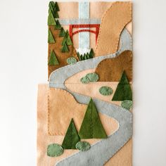 a piece of art made out of felt with trees, mountains and a river running through it