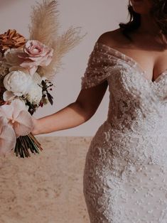 a woman in a wedding dress holding a bridal bouquet with flowers on the side