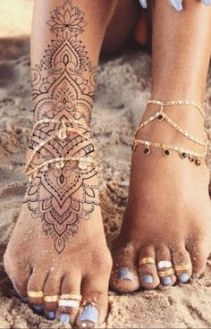 a woman's feet with tattoos and jewelry on the sand in front of her