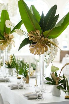 the table is set with white and gold place settings, greenery and silverware