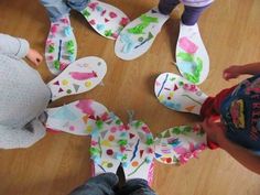 several children are standing in a circle with paper cut outs on the floor and one child is wearing a blue t - shirt