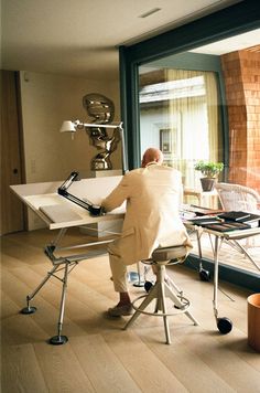 a man sitting at a desk in front of a window looking out on the outside