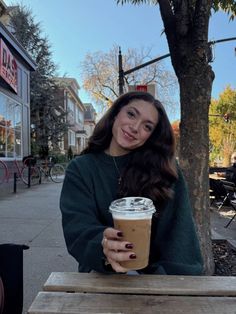 a woman sitting at a table with a cup of coffee in her hand and smiling