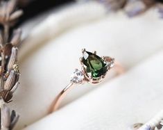 an engagement ring with a green stone surrounded by small white diamonds on top of it