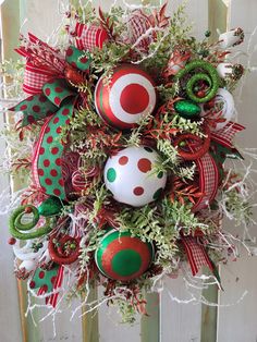 a christmas wreath with ornaments hanging from it's side on a wooden fence in front of a door