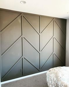 a bed sitting next to a gray wall with wooden paneling on top of it