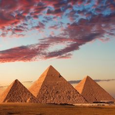 three pyramids in the desert under a cloudy sky with pink and blue clouds above them