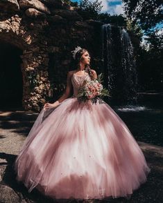 a woman in a pink ball gown standing next to a waterfall wearing a tiara