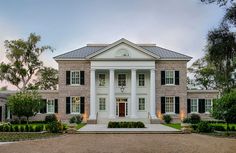 a large white house with black shutters on the front and side windows, surrounded by greenery