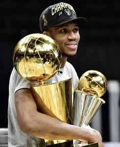 the basketball player is holding two trophies in his hands and smiling at the camera while standing next to him