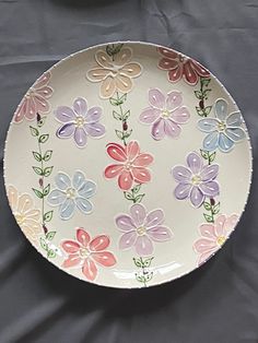 a plate with flowers painted on it sitting on a gray tableclothed surface next to a bowl