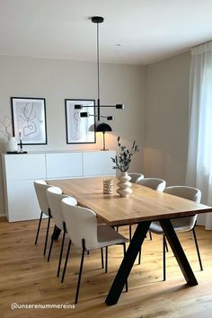 a dining room table with white chairs and a vase on it's end, in front of a window