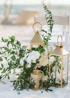 an arrangement of white flowers and greenery on a chair with two lanterns in the snow