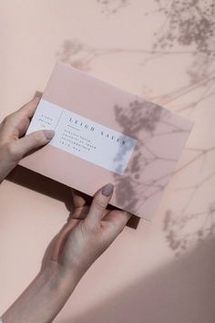 a person holding up a business card in front of a pink wall with shadows on it