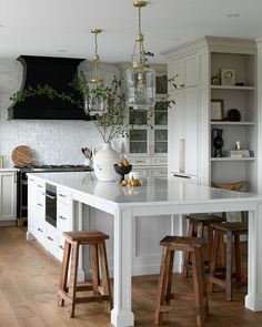 a white kitchen with wooden stools and an island in front of the stove top