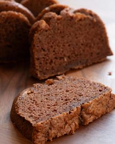 a loaf of brownie sitting on top of a wooden table next to sliced bread