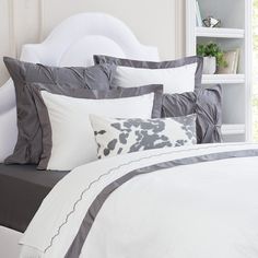 a bed with grey and white sheets and pillows