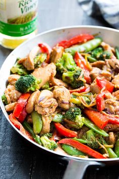 a skillet filled with chicken and veggies next to a bottle of beer