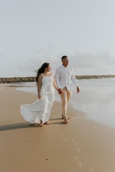 a man and woman walking on the beach holding hands