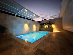 an outdoor swimming pool at night with lights on the wall and ceiling lighting above it