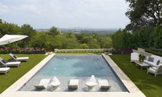 an outdoor swimming pool with lounge chairs and umbrellas on the grass next to it