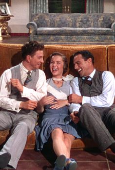 three people laughing while sitting on a couch