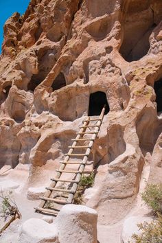 a ladder leading up to a cave entrance in the desert with large rocks and boulders